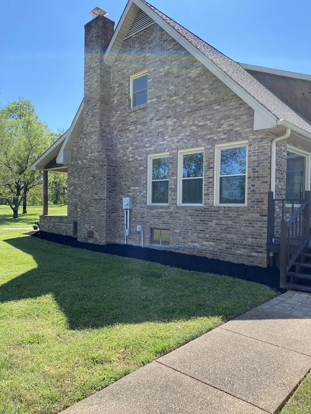 view of side of home featuring brick siding, a chimney, and a yard