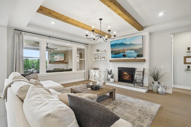 living room featuring ceiling fan with notable chandelier, light hardwood / wood-style flooring, a large fireplace, and beam ceiling