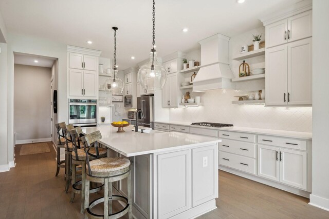 kitchen with light wood-type flooring, backsplash, appliances with stainless steel finishes, sink, and a center island with sink