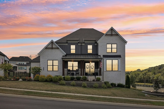 modern farmhouse featuring brick siding, a porch, a front yard, a standing seam roof, and metal roof