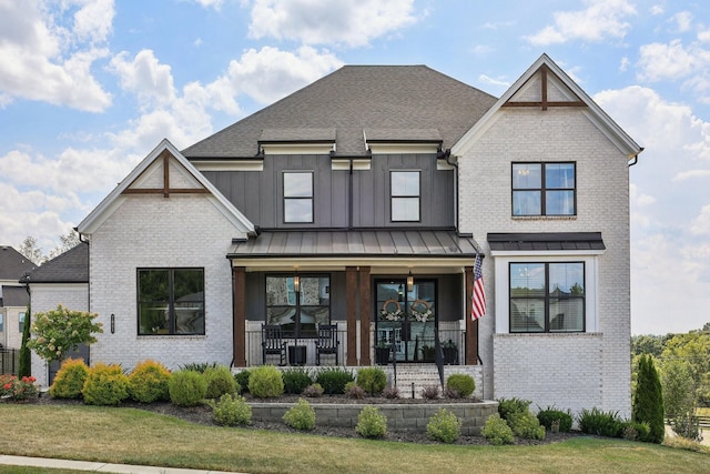 view of front of property featuring covered porch, brick siding, board and batten siding, a front lawn, and a standing seam roof