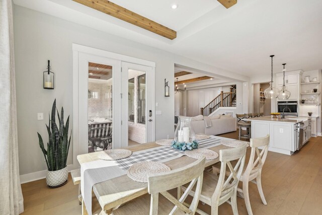 dining area featuring sink, beam ceiling, and light wood-type flooring