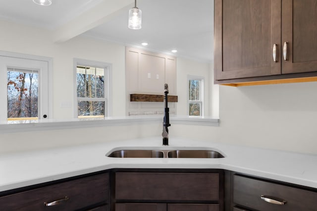 kitchen with sink, ornamental molding, decorative light fixtures, beam ceiling, and dark brown cabinetry