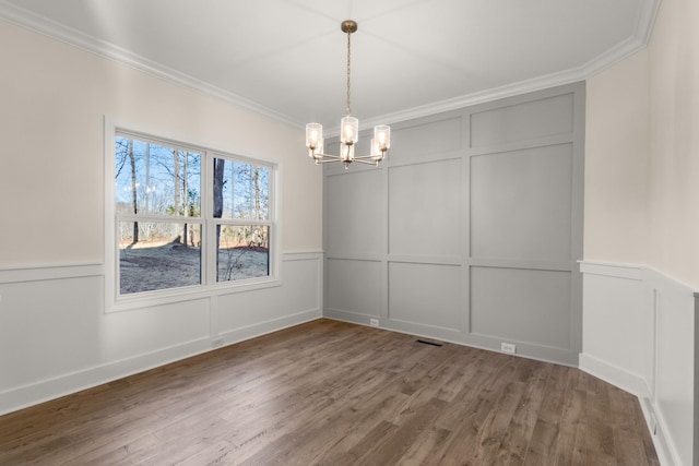 unfurnished dining area featuring dark hardwood / wood-style flooring, crown molding, and a chandelier