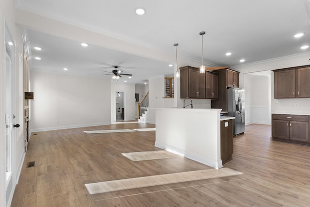 kitchen with dark brown cabinets, decorative light fixtures, a center island with sink, stainless steel fridge with ice dispenser, and light hardwood / wood-style floors