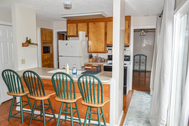 kitchen featuring a textured ceiling, white appliances, hardwood / wood-style floors, and range hood