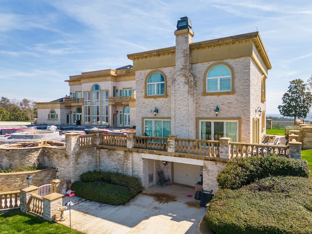 rear view of property with a garage, concrete driveway, a chimney, and a balcony