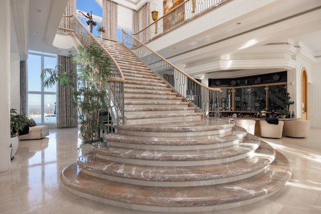 staircase with tile patterned flooring, crown molding, and a high ceiling