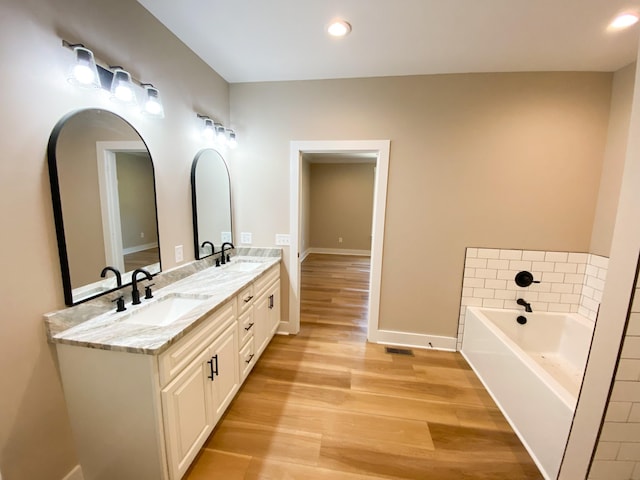 full bath featuring double vanity, a garden tub, a sink, and wood finished floors