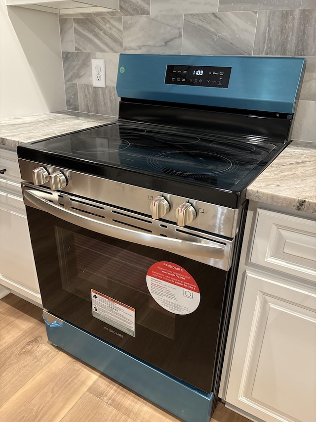 interior details featuring light wood-style flooring, stainless steel electric range, backsplash, and white cabinetry