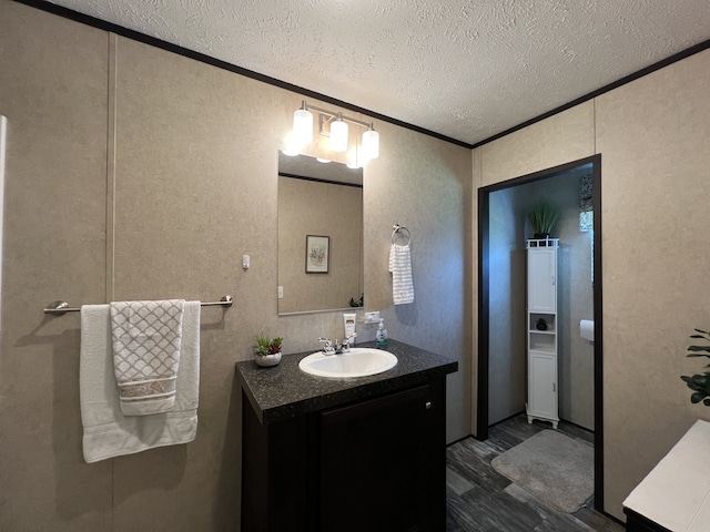 bathroom featuring a textured ceiling, ornamental molding, vanity, and hardwood / wood-style flooring