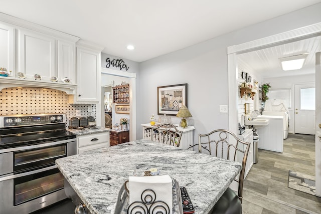 kitchen with backsplash, stainless steel electric stove, white cabinets, light stone counters, and light tile patterned floors