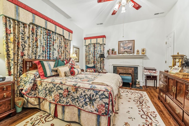 bedroom featuring a fireplace with flush hearth, visible vents, ceiling fan, and wood finished floors