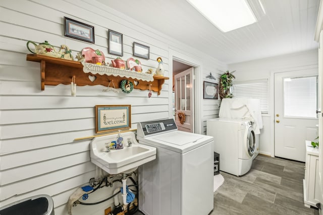 clothes washing area with independent washer and dryer, wooden walls, and sink