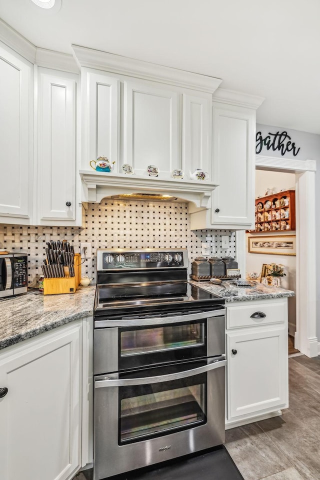 kitchen featuring tasteful backsplash, white cabinets, appliances with stainless steel finishes, light stone countertops, and premium range hood