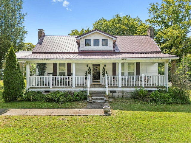 country-style home with covered porch, a chimney, metal roof, and a front yard