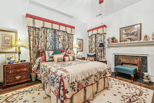 bedroom with light wood-type flooring, visible vents, a fireplace, and ceiling fan