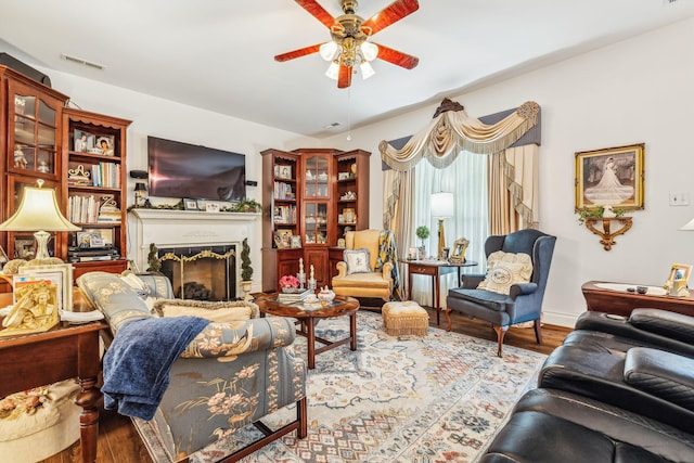 living area featuring a ceiling fan, visible vents, a fireplace, and wood finished floors