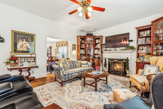 living room with baseboards, a lit fireplace, a ceiling fan, and wood finished floors