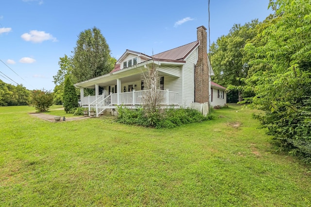 view of front of home featuring metal roof, a porch, a front lawn, and a chimney