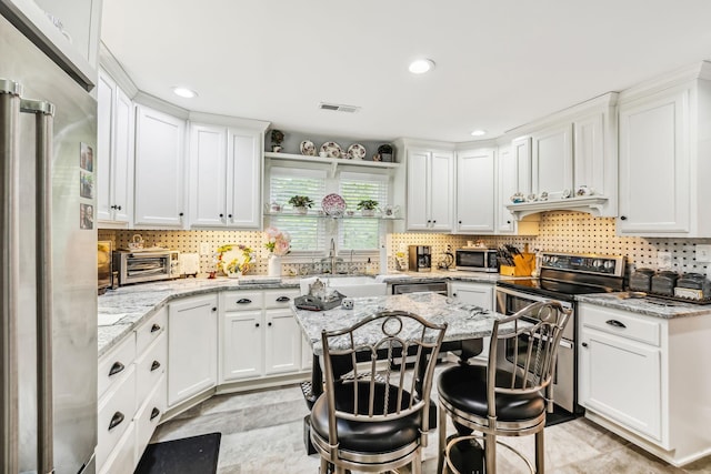 kitchen with visible vents, light stone counters, stainless steel appliances, white cabinetry, and a sink