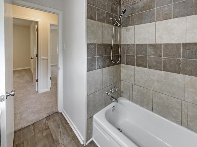 bathroom featuring baseboards, wood finished floors, and bathing tub / shower combination