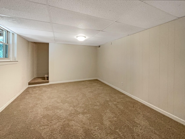 below grade area with carpet floors, wood walls, baseboards, and a paneled ceiling