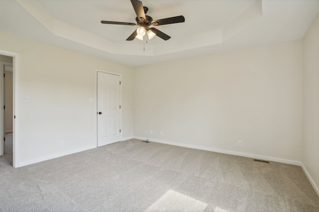 unfurnished room with ceiling fan, a raised ceiling, and light carpet