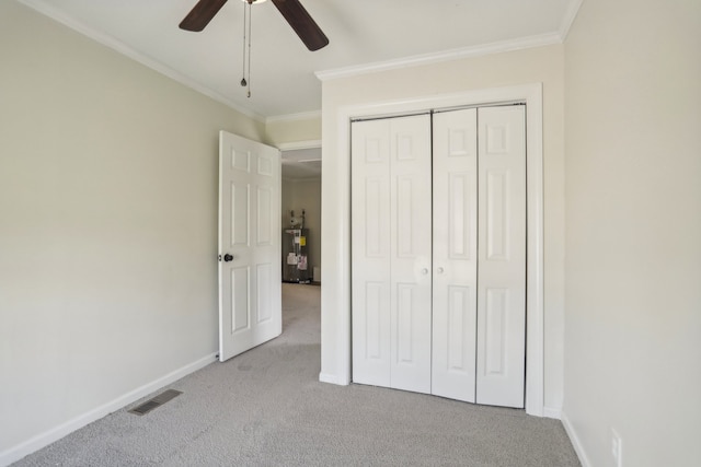 unfurnished bedroom with crown molding, electric water heater, carpet flooring, ceiling fan, and a closet