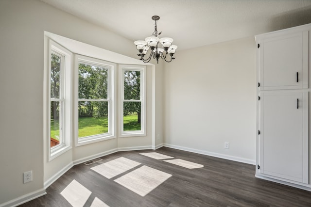 spare room featuring dark wood-type flooring and a notable chandelier