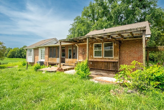 rear view of house with central AC unit and a lawn