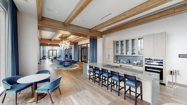 kitchen with a chandelier, beamed ceiling, a kitchen breakfast bar, light stone countertops, and tasteful backsplash