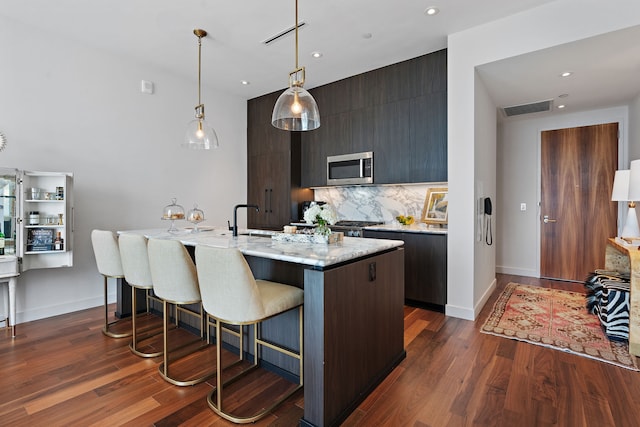 kitchen with a kitchen bar, decorative backsplash, light stone countertops, an island with sink, and dark hardwood / wood-style floors