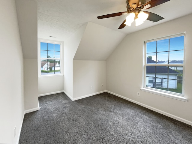 bonus room featuring ceiling fan, a textured ceiling, lofted ceiling, and dark colored carpet