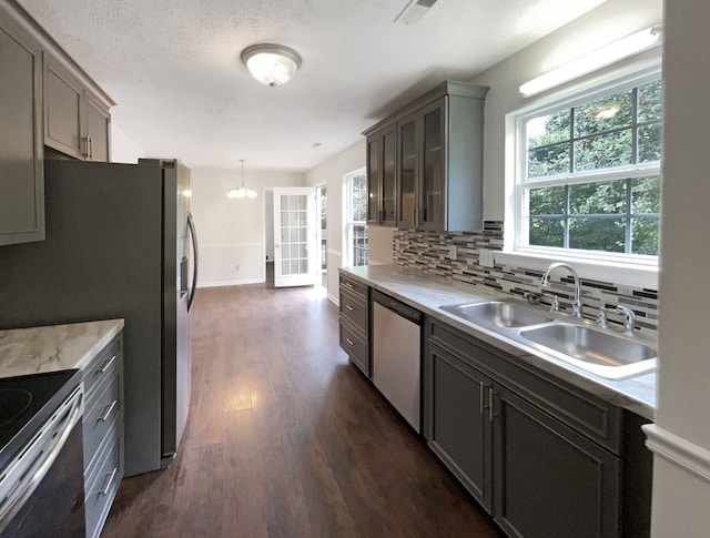 kitchen with decorative backsplash, stainless steel dishwasher, dark hardwood / wood-style flooring, hanging light fixtures, and sink