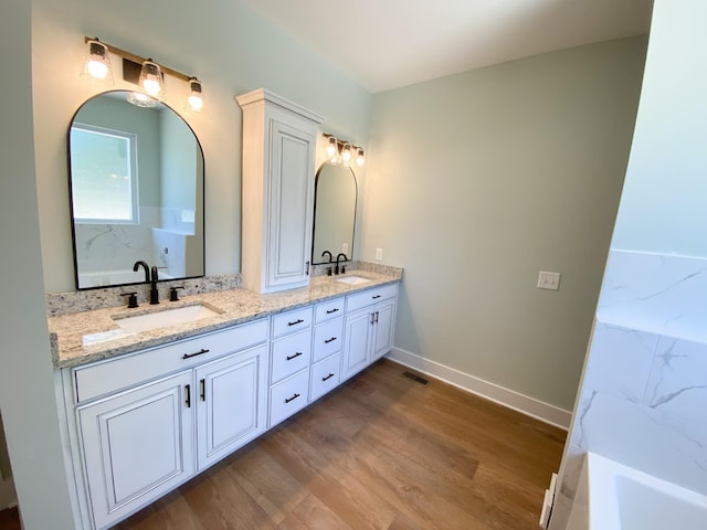 bathroom with double vanity, baseboards, a sink, and wood finished floors