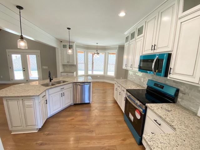 kitchen with glass insert cabinets, appliances with stainless steel finishes, hanging light fixtures, white cabinetry, and a sink