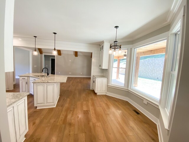 kitchen with sink, decorative light fixtures, light stone counters, light hardwood / wood-style floors, and a center island with sink