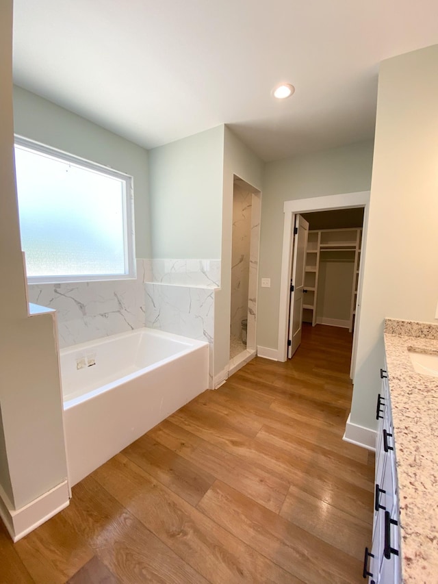 full bath featuring a walk in closet, wood finished floors, vanity, a walk in shower, and a bath