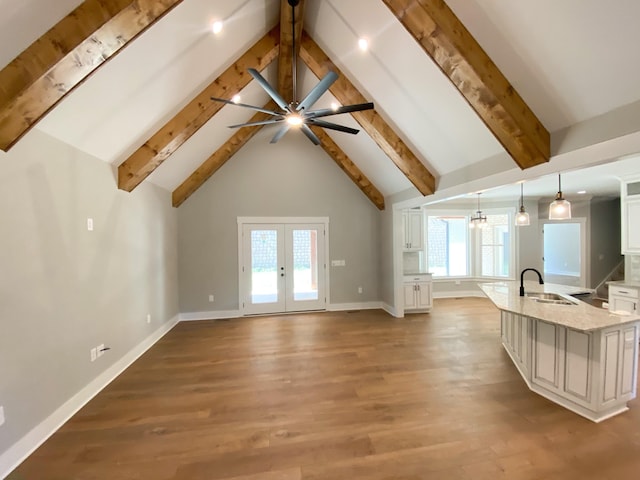 unfurnished living room with beam ceiling, a sink, light wood finished floors, and french doors