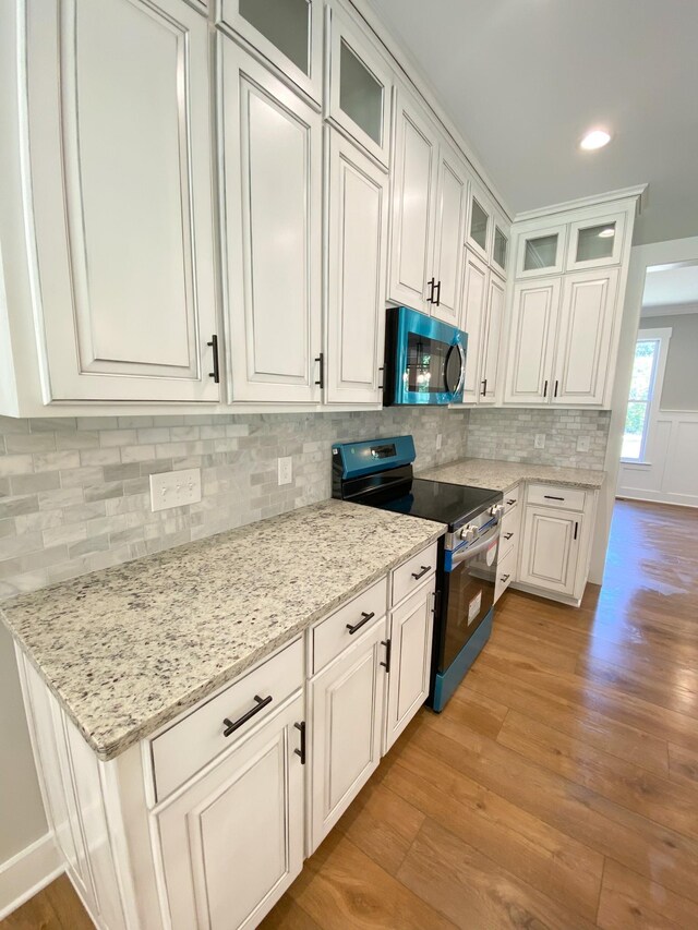 kitchen featuring appliances with stainless steel finishes, light hardwood / wood-style flooring, decorative backsplash, light stone countertops, and white cabinetry