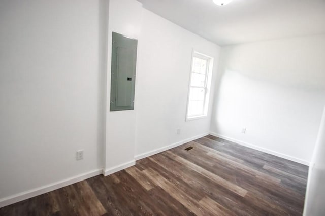 empty room with dark wood-type flooring, electric panel, and baseboards