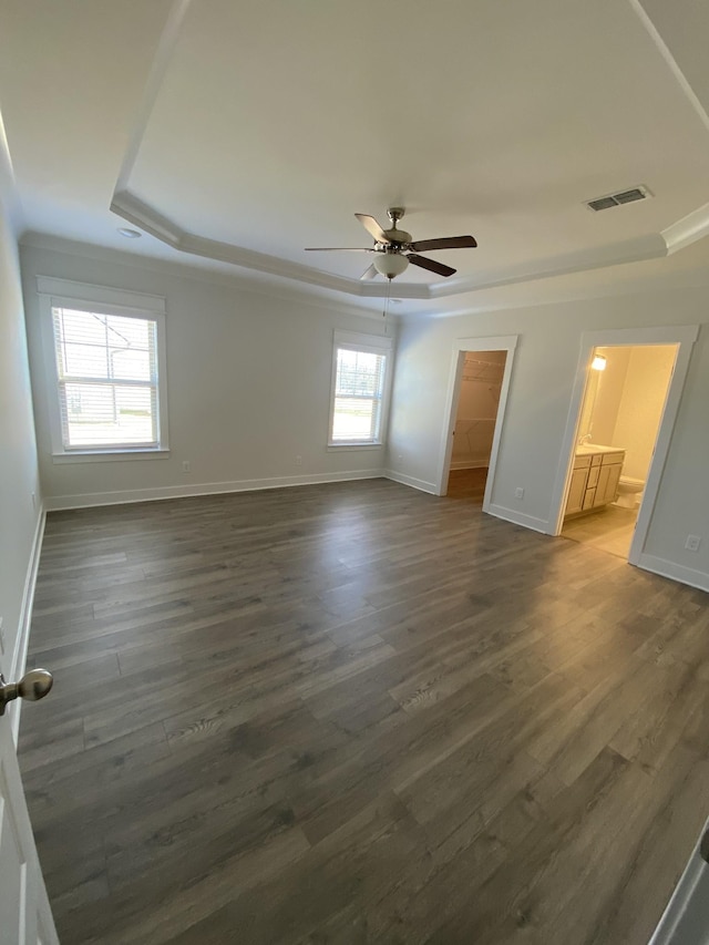 unfurnished room featuring a raised ceiling, ceiling fan, dark wood-type flooring, and a healthy amount of sunlight