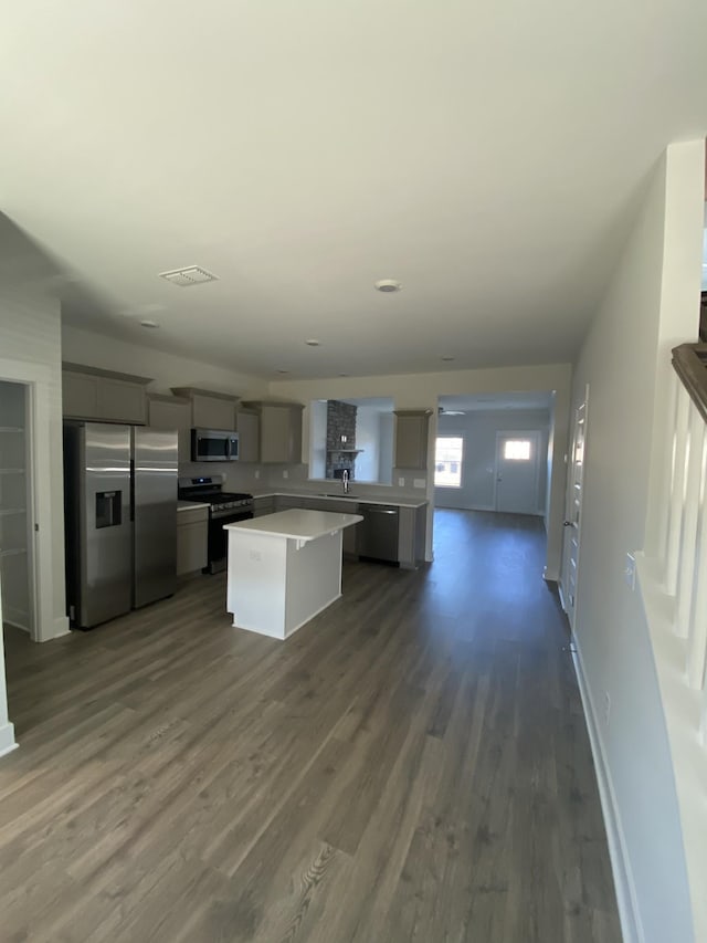 kitchen with sink, dark wood-type flooring, gray cabinets, a kitchen island, and appliances with stainless steel finishes