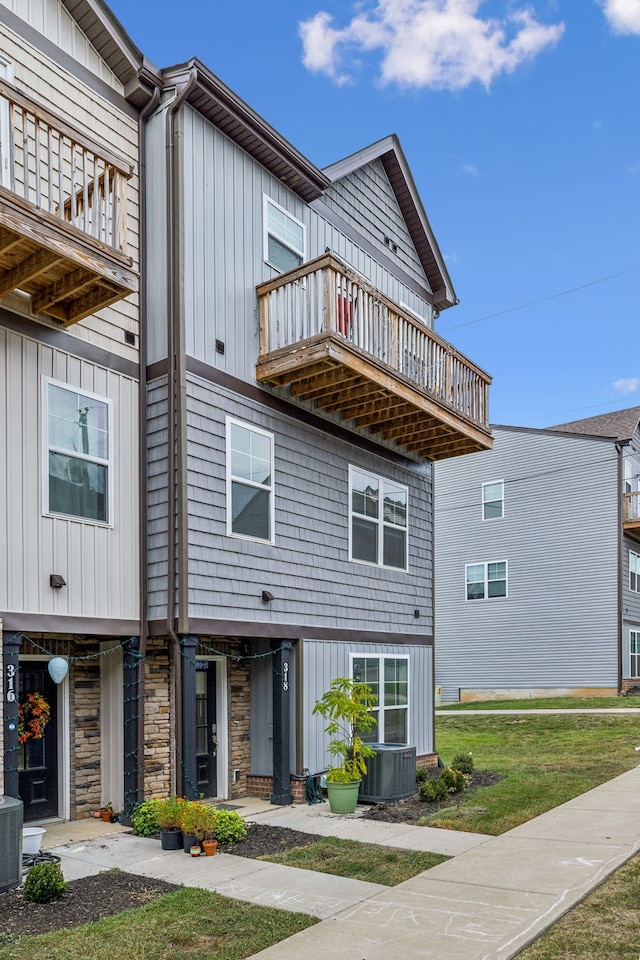 view of property with a balcony, a front yard, and cooling unit