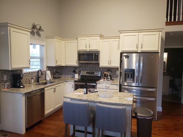 kitchen with sink, light stone counters, a center island, stainless steel appliances, and decorative backsplash