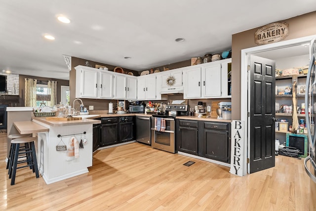 kitchen with appliances with stainless steel finishes, light hardwood / wood-style floors, sink, white cabinets, and a kitchen breakfast bar