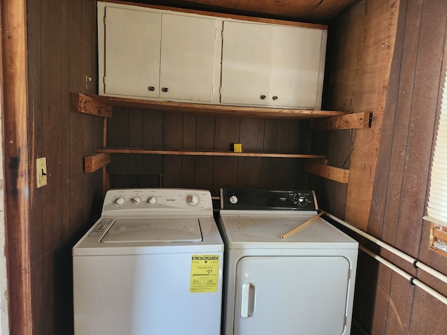 laundry room featuring wood walls, washing machine and dryer, and cabinets