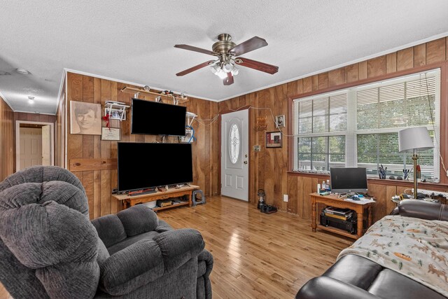 living room featuring light wood-type flooring, a textured ceiling, ceiling fan, and wooden walls