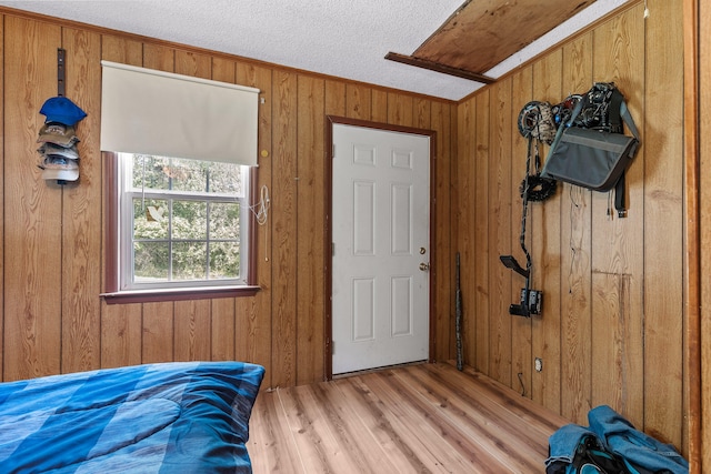 bedroom featuring a textured ceiling, crown molding, light wood-type flooring, and wooden walls